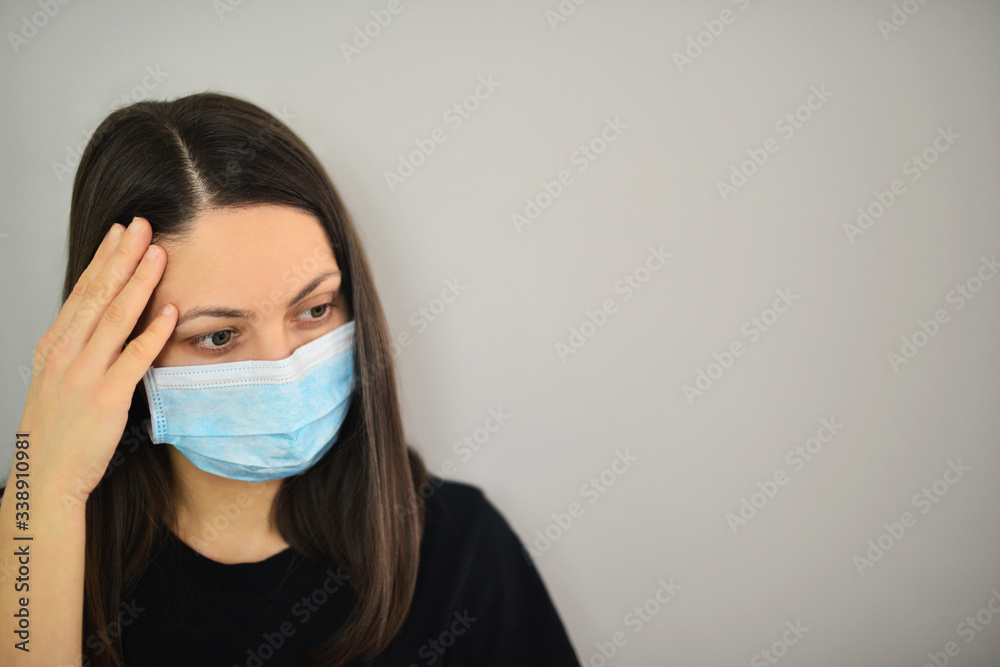 Young woman wearing medical mask, holding her head with hand.