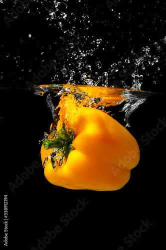 Big yellow bell pepper falls into the water.Fresh yellow paprika splash in water on black background