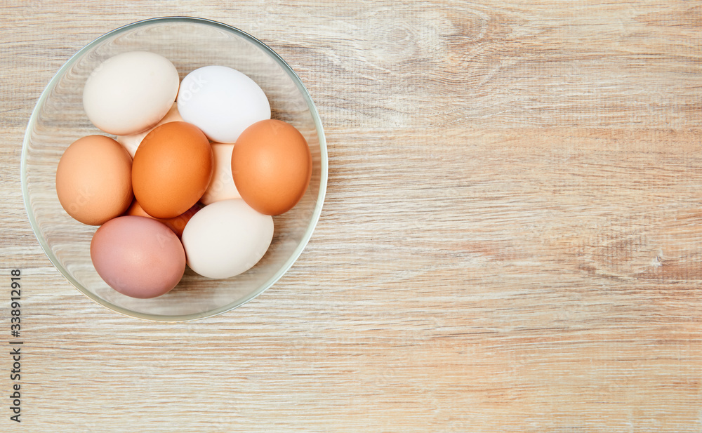 eggs of different colors from white to brown in a glass bowl on a wooden table surface