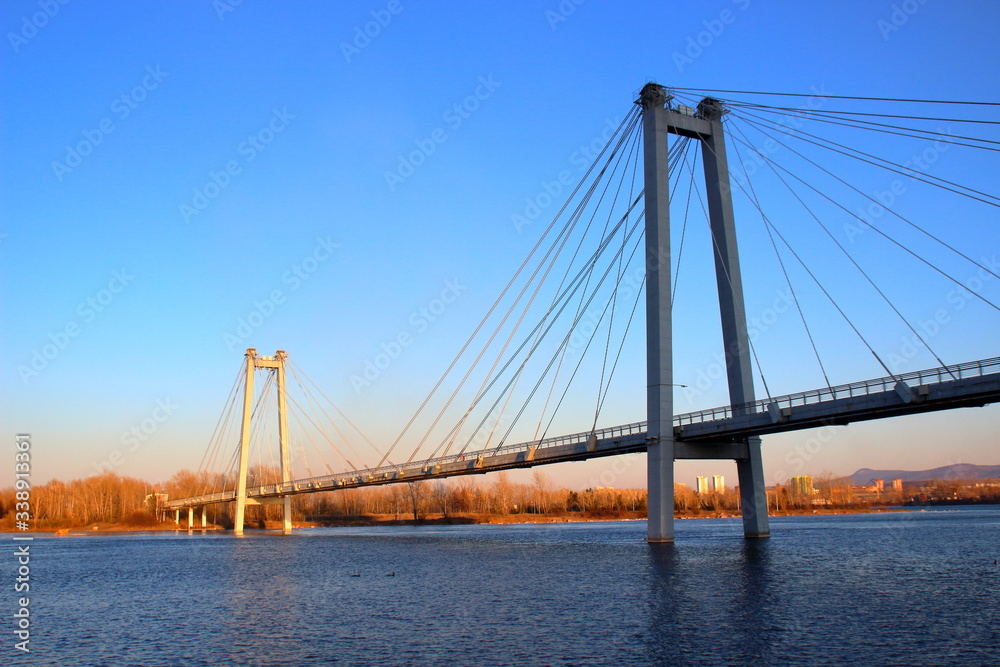 Fototapeta premium Sunset view of the foot Vinogradovsky (cable-stayed) bridge through the Yenisei river on Tatyshev island in Krasnoyarsk, Russia
