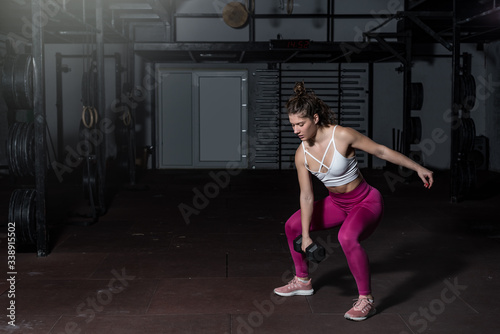 Young strong fit muscular sweaty girl with big muscles strength cross workout training with dumbbells weights in the gym dark image with shadows real people exercise