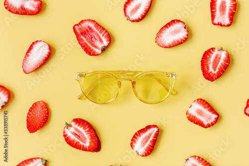 Yellow glasses on a colored background surrounded by strawberries.