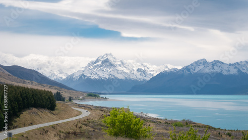 Alpine vista with turquoise lake and mountains (with Mount Cook) in backdrop with highway leading towards them, shot at Aoraki/Mt Cook National Park, New Zealand