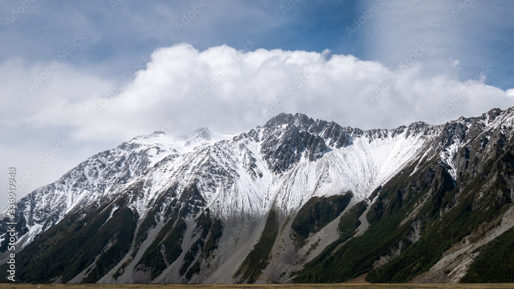 Mountain range with puffy clouds above partially lit by sun. Shot at Aoraki / Mt Cook National Park, New Zealand