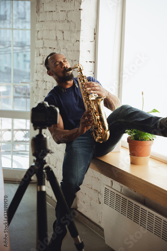 African-american musician playing saxophone during online concert at home isolated and quarantined. Using camera  laptop  streaming  recording courses. Concept of art  support  music  hobby  education