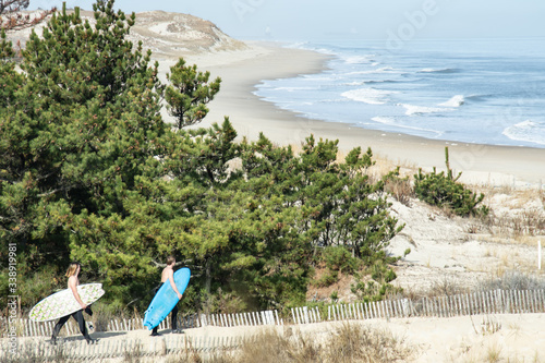 Two surfers walk trail to beach in front of great dune at Herring Point, Cape Henlopen State Park, Delaware
