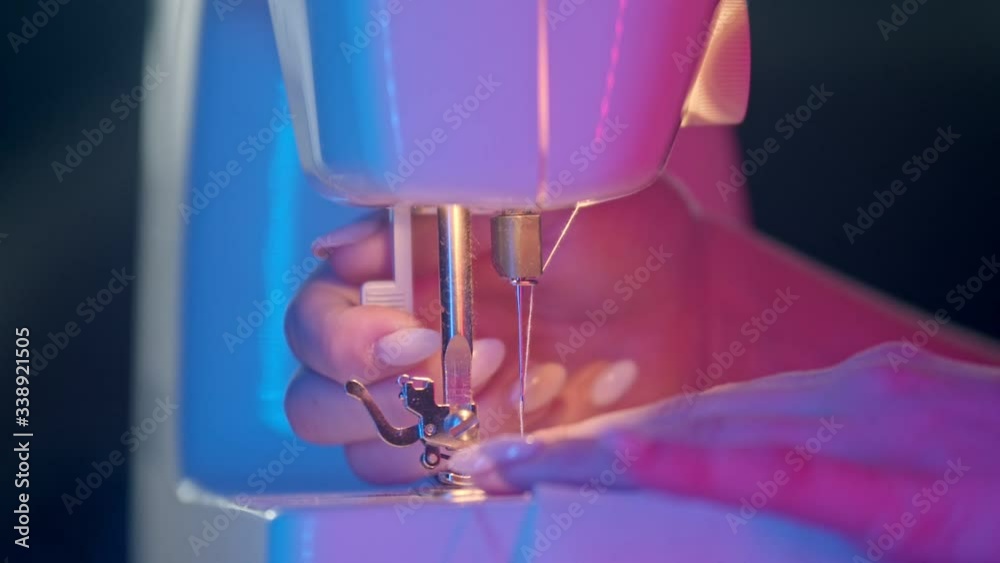 Hands of seamstress sewing a white cloth using a sewing machine in neon lighting