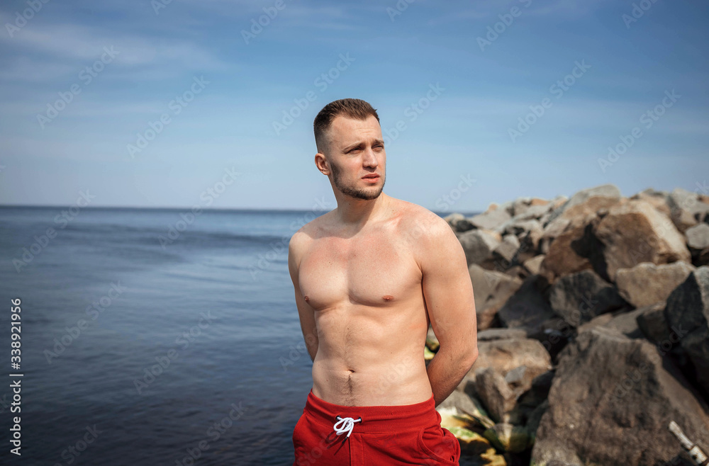 Young guy on the sandy beach with a wooden bridge in red shorts, topless