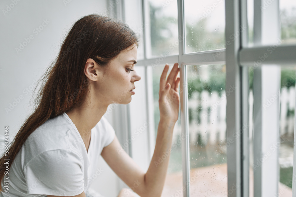 A woman at home looks out the window with a pensive look