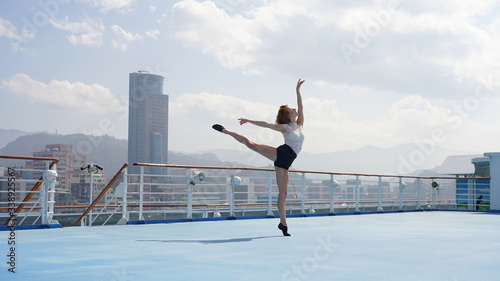 Elegant dancer. Beautiful slim sports model. Beautiful girl with long legs performs a dance pose balancing on one leg and toes. Woman on a cruise ship against the background of the Asian port city