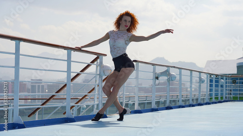 Sporty red-haired girl on the walking deck of a cruise ship. Flexible European dancer performs elements on a sunny day against the background of an Asian city. jumping, twine