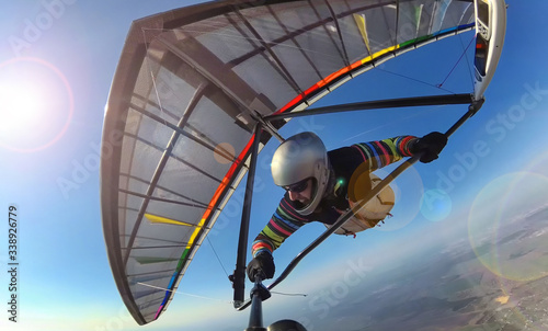 Hang glider pilot on colorful wing makes photo selfie high above ground.