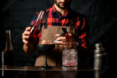 Man bartender pours red liquid from jigger into mixing cup