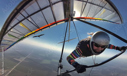 Hang glider pilot on colorful wing flies together with eagle.