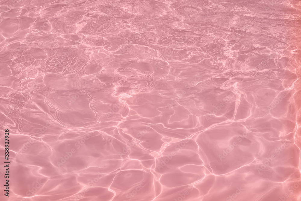Closeup of calm clear water surface with water splashes in trendy pink color. Swimming pool water texture. Trendy fresh abstract nature background. 2020 color trend concept.
