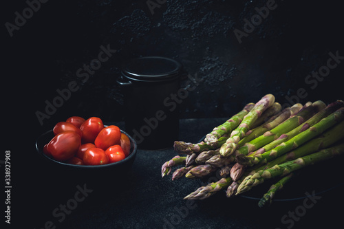Green asparagus and small red tomatoes on a dark background.