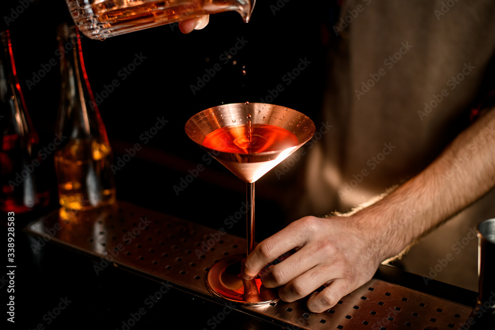 Close-up metal martini glass in which bartender pours cocktail.