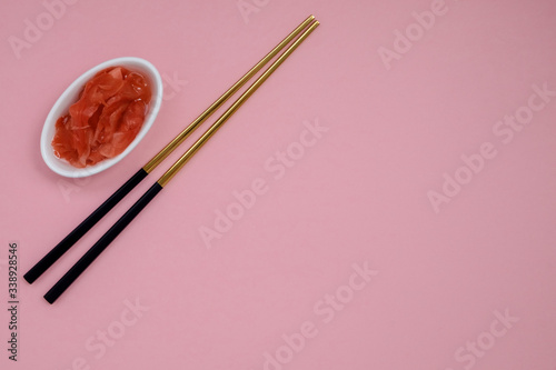 Marinated ginger and chopsticks with black handles, folded cross on a pink background. Flat lay with copy space, selective focus. Japanese food. Horizontal orientation.