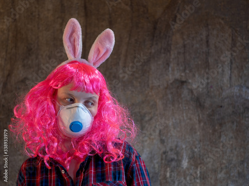 Attractive girl in pink wig and medical mask in plaid shirt, pink jacket and carnival ears of hare. Beautiful middle aged woman with cancer without hair