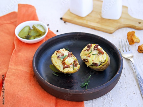 Twice baked potatoes with cheese and chanterelle mushrooms on a brown clay plate on a light concrete background. Recipes with potatoes. Cooking wild mushrooms.