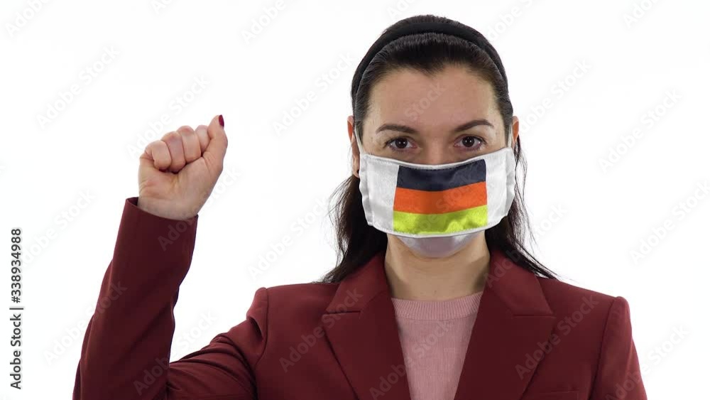 Virus and disease prevention concept. Woman wears a protective medical mask with the image of the flag of Germany. Shows the solidarity with the closed fist hand gesture. Demonstrate solidarity sign. Virus and disease prevention concept. Woman wears a protective medical mask with the image of the flag of Germany. Shows the solidarity with the closed fist hand gesture. Demonstrate solidarity sign.