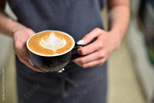 Female barista hands and a large cup of coffee with a pattern on the surface.