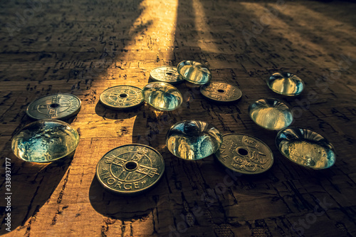 Closeup of a pile of Norwegian money on a cork background, illuminated by a beam of sunlight.