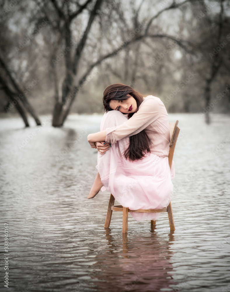 Fototapeta premium Self-isolation in quarantine. The girl sits on a chair in the water. Pandemic, flood