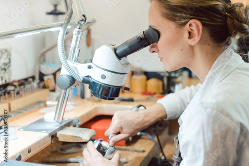 Diligent jeweler working on microscope at her workbench