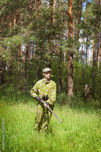 Hunter dressed in camouflage and with shotgun is walking through forest