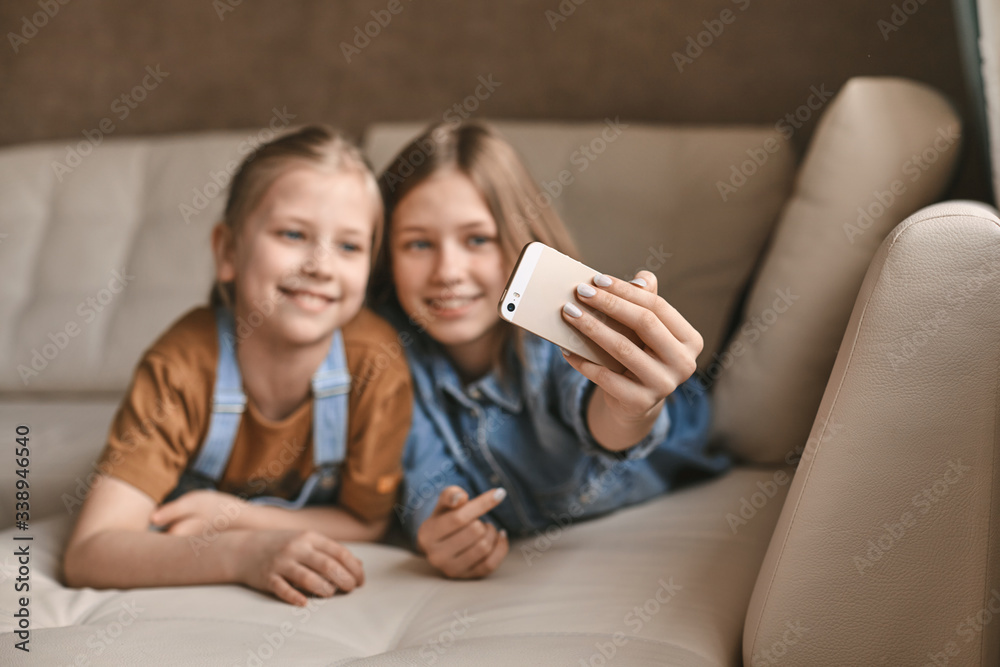 Beautiful girls take selfies on their phone while lying on the sofa. Sisters take a break from homework and take photos during quarantine Beautiful girls take selfies on their phone while lying on the sofa. Sisters take a break from homework and take photos during quarantine