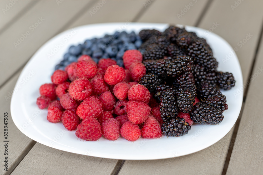 White ceramic plate with assorted sweet juicy organic seasonal berries for snack. Ripe tasty fresh raspberry, blackberry and blueberry summer mix for breakfast morning. Healthy vitamin nutrition diet White ceramic plate with assorted sweet juicy organic seasonal berries for snack. Ripe tasty fresh raspberry, blackberry and blueberry summer mix for breakfast morning. Healthy vitamin nutrition diet
