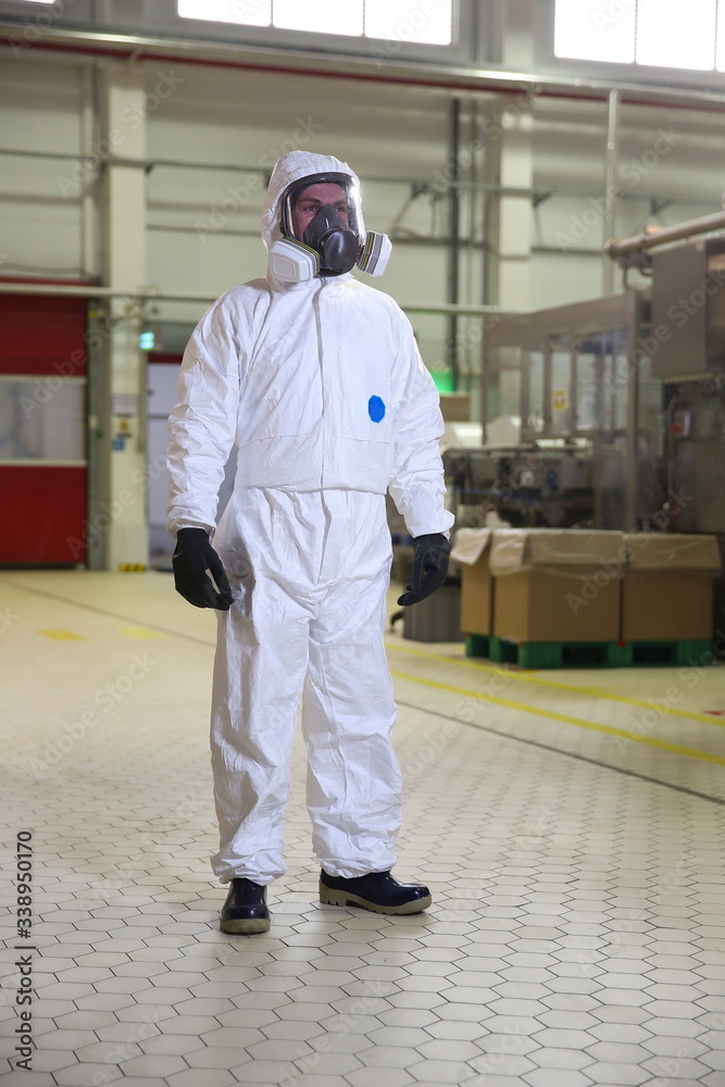 worker male in white protective suit and gas mask standing in the workshop of a factory