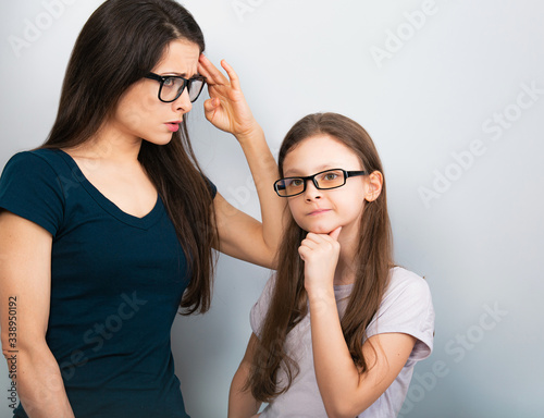 Serious thinking mother and sad doubt kid in glasses on light blue background. Closeup studio portrait. Teaching kids staying at home. Online education. Distance learning