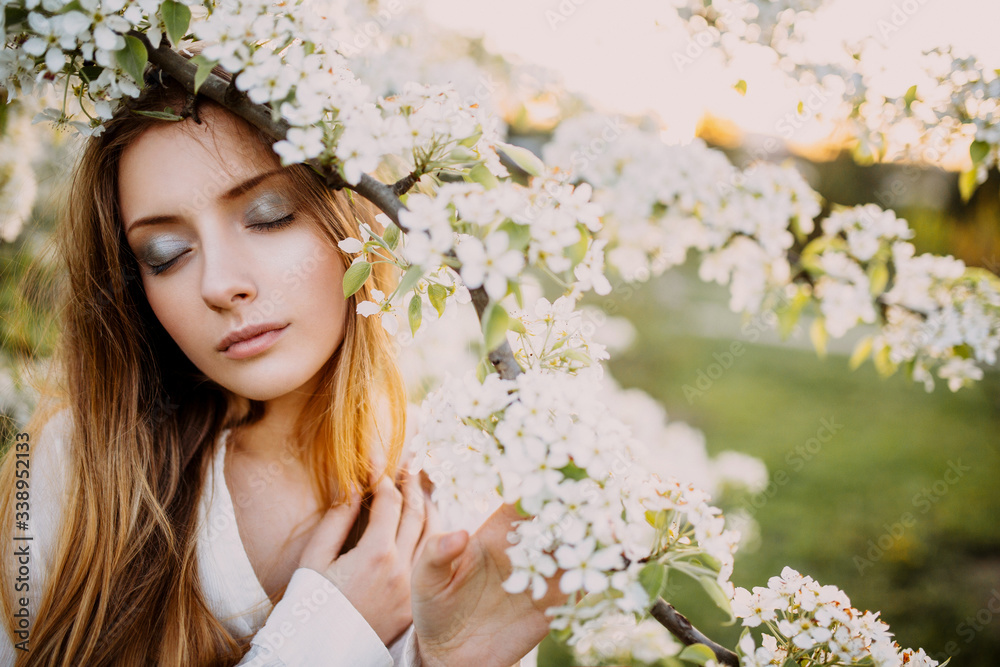 Portrait of a beautiful blonde young woman on a spring day with white flowers of a cherry tree.