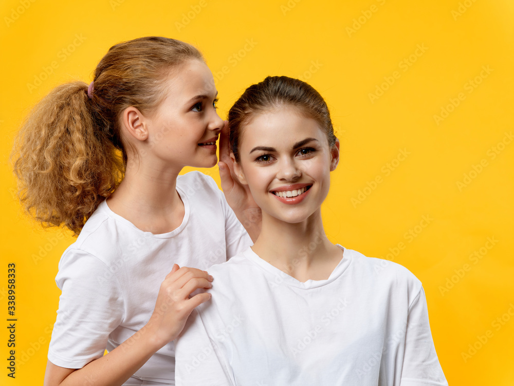 Cheerful Mom and daughter in white t-shirts chatting joy yellow studio background Cheerful Mom and daughter in white t-shirts chatting joy yellow studio background