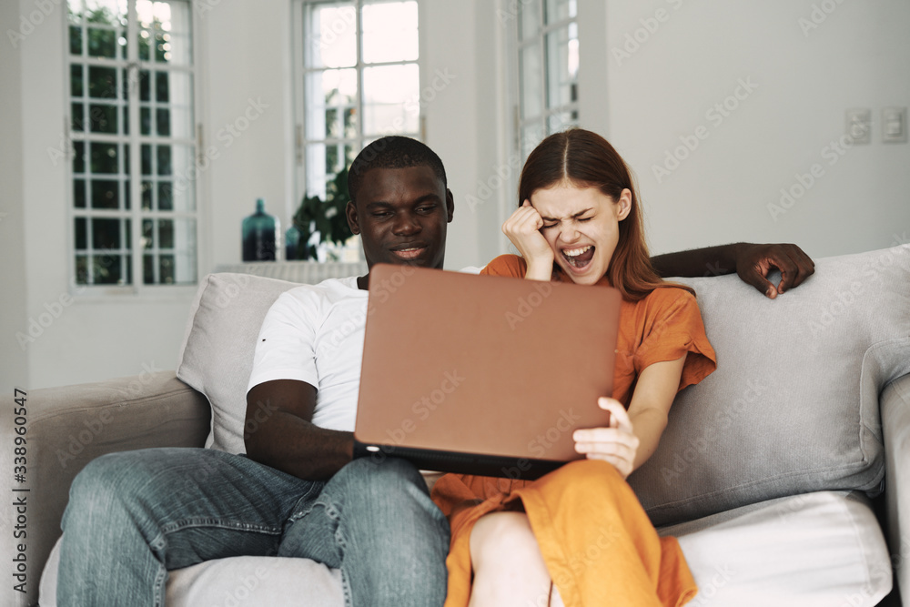 Cheerful young couple at home on the couch in front of a laptop watching a movie Cheerful young couple at home on the couch in front of a laptop watching a movie