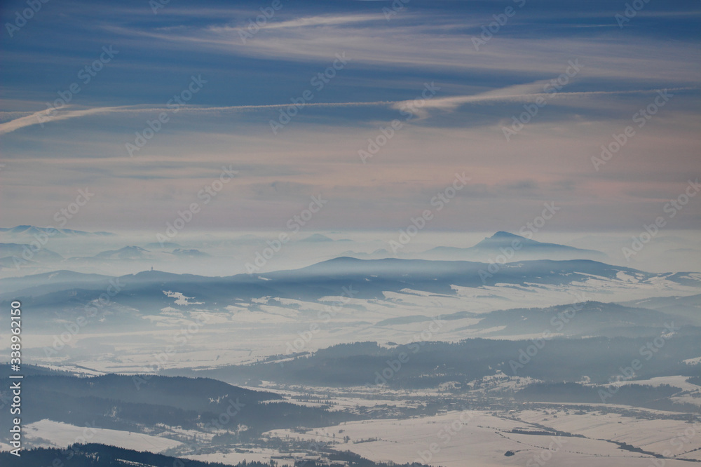 Frozen winter landscape with blue mountain ridges, snowy hazy valleys and conical Velky Choc peak in fog layers Orava Liptov regions Oravska Magura Chocske vrchy ranges Slovakia Eastern Central Europe