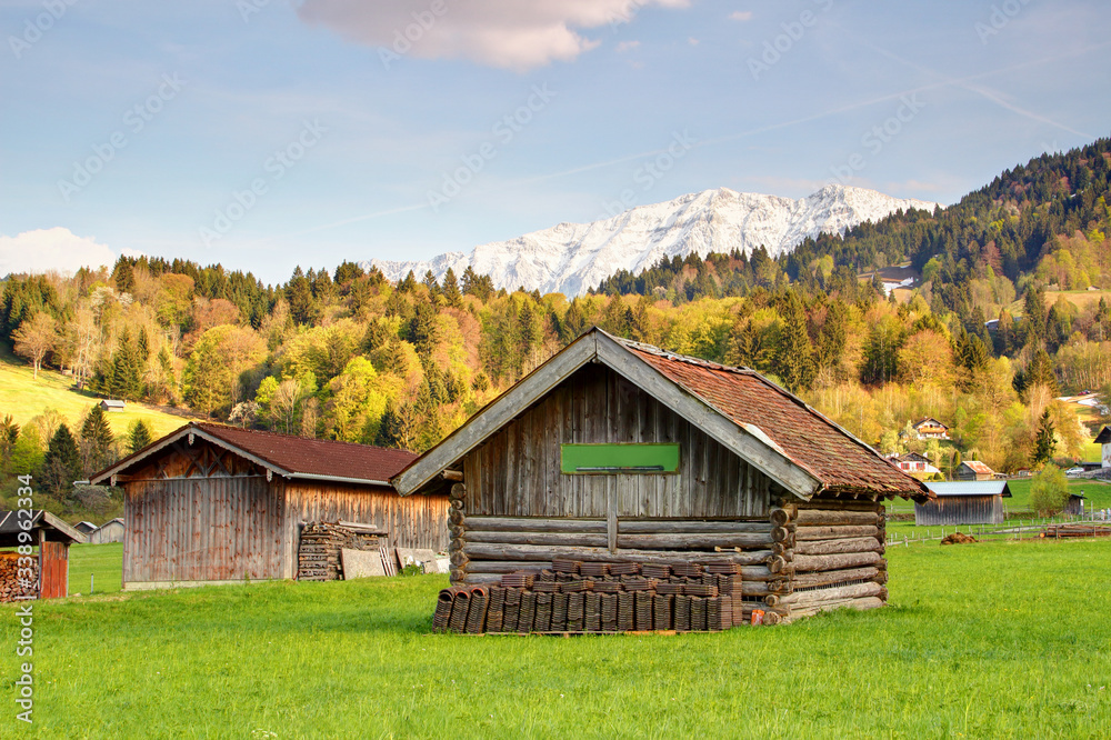 Bavarian rural scenery of typical timber hay barns with sunny forests and snowy peaks of Wetterstein mountain range in background, Hausberg Garmisch Partenkirchen Bayern Germany Europe