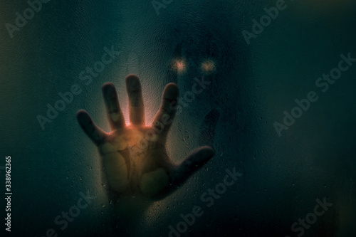 Horror scene of a man with bloody hand against wet shower glass. Toned image. Horror concept