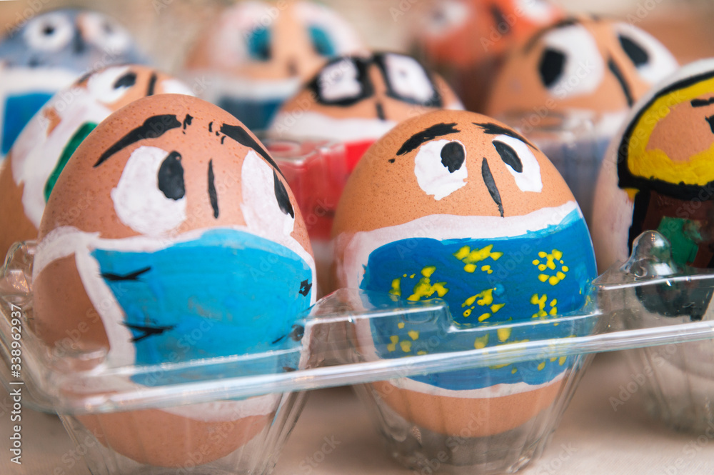 Close up. Easter during coronavirus. Eggs painted as faces with medical masks.