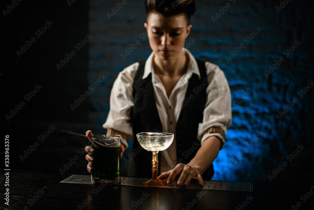 bartender's hands on glass and mixing cup with green cold cocktail stand on bar counter