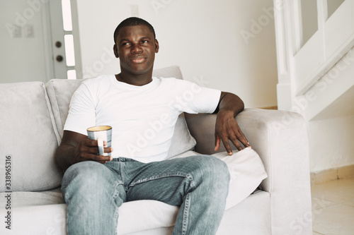 A man of African appearance at home on the couch relaxing a cup of drink