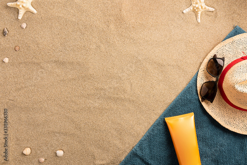 Summer vacation composition. Hat, sun cream and sunglasses on sand background. Harsh light with shadows. Summer background. Border composition made of towel