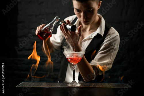 professional bartender pours drink into glass which standing on burning bar counter