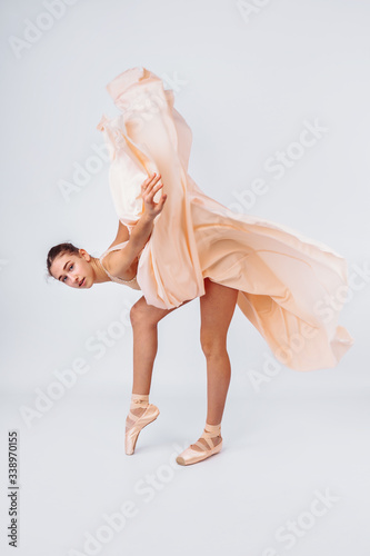 A young and incredibly beautiful ballerina is posing and dancing in a white studio full of light. The beauty of classical ballet art. Graceful ballerina dancing, posing in tender peach tutu
