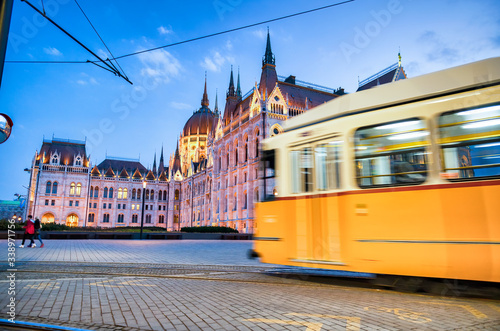 Old yellow tram speeds up along city streets at night. The historical center of the capital of Hungary