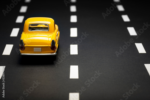 Rear view of a Yellow toy car on an asphalt road