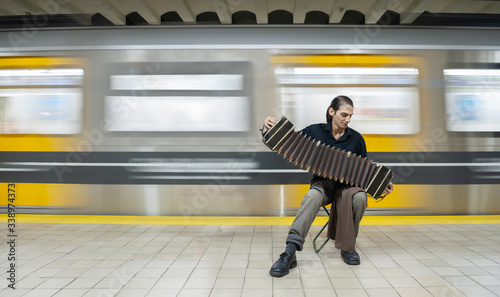 Tango performer playing a bandoneon with hat and subway in motion.
