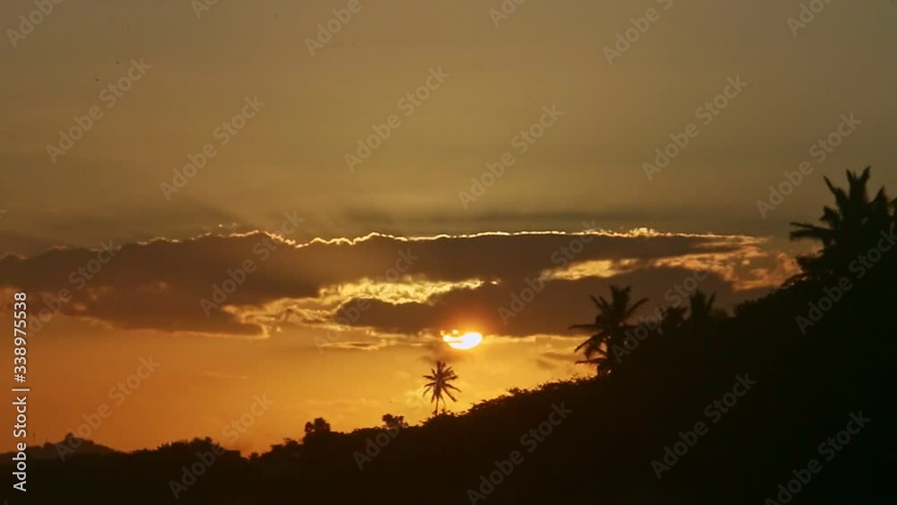 yellow sun setting down behind big clouds and palm trees silhouettes on seashore yellow sun setting down behind big clouds and palm trees silhouettes on seashore